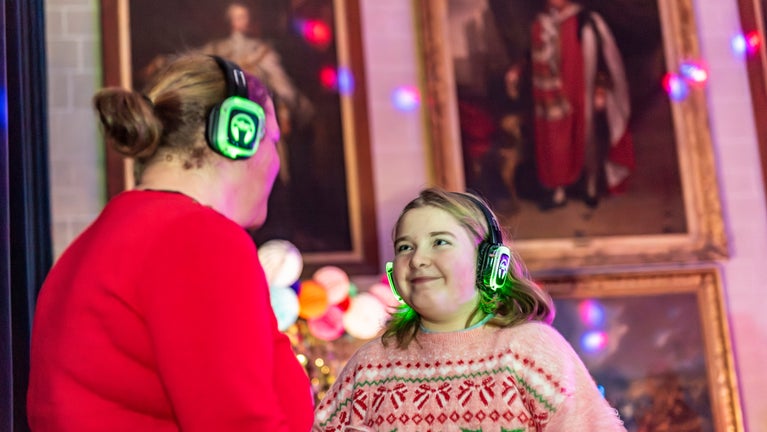 People with headphones on and Christmas jumpers at silent disco at Plas Newydd with portraits in background